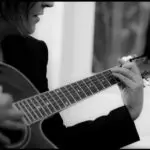 Sabine Noël jouant de la guitare acoustique, photo en noir et blanc capturant un moment intime et musical
